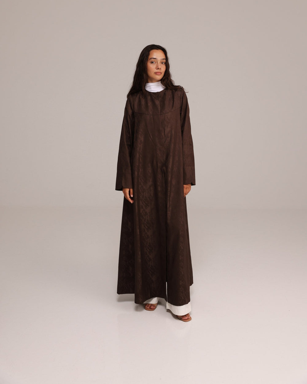 Woman wearing a brown long-sleeve dress against a plain background