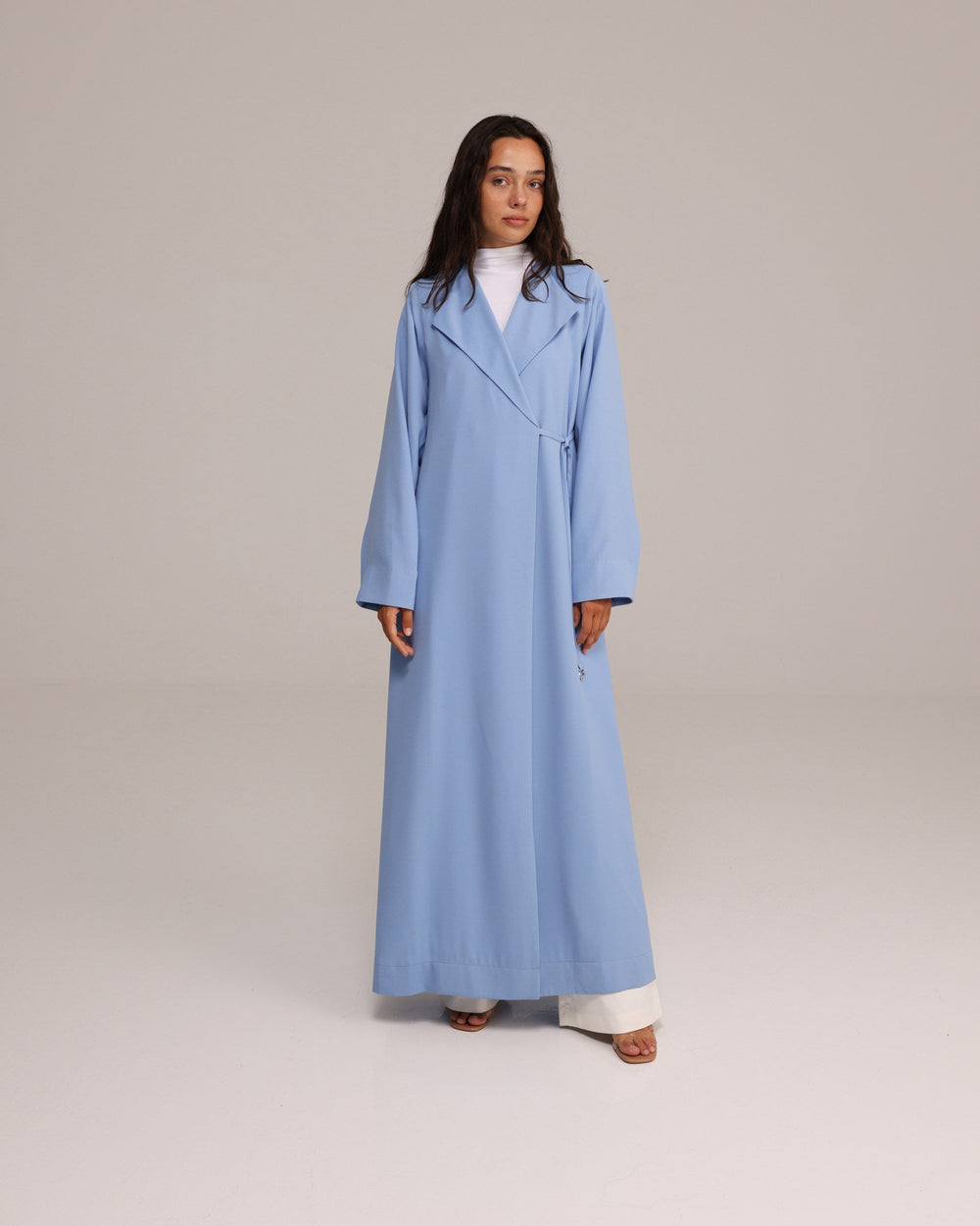 Woman wearing a long light blue coat on a plain background