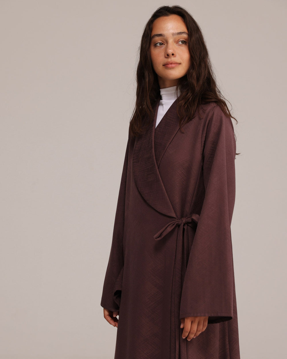 Woman wearing a long brown coat against a plain background