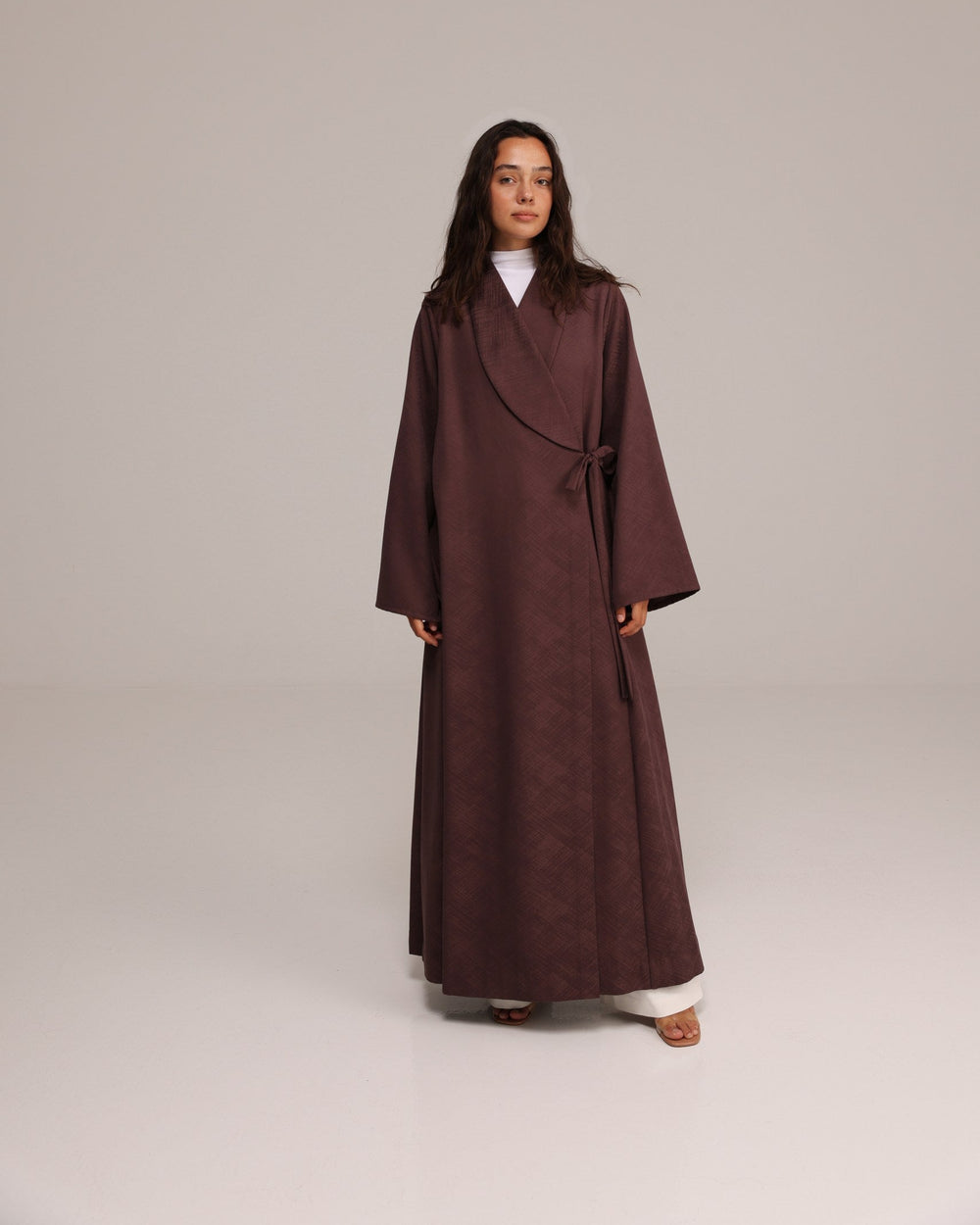 Woman wearing a long brown coat on a plain background