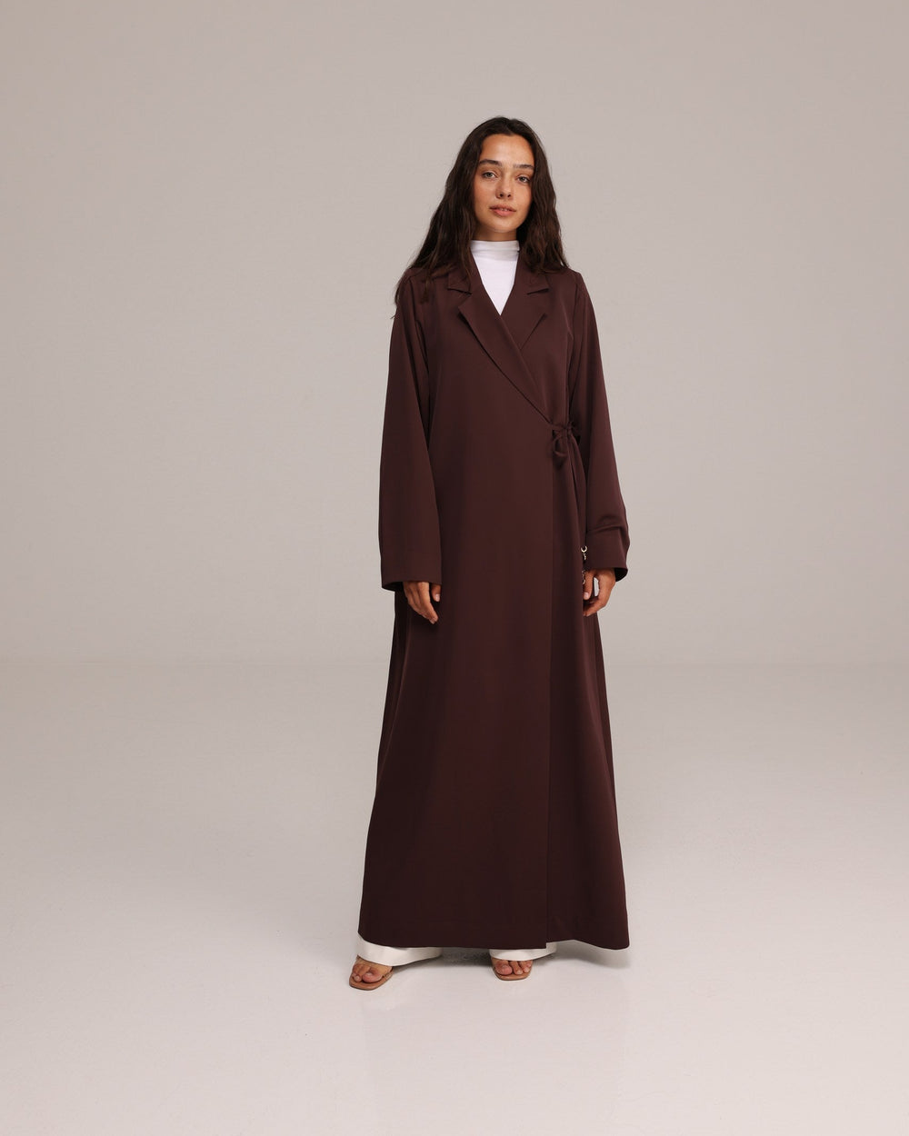 Woman wearing a long brown coat on a plain background