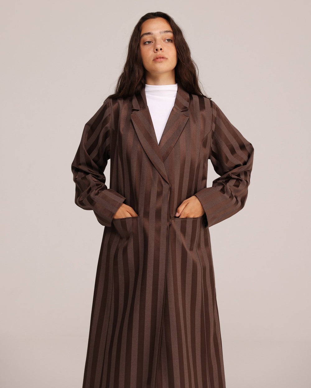 Woman wearing a long brown coat over a white top on a plain background