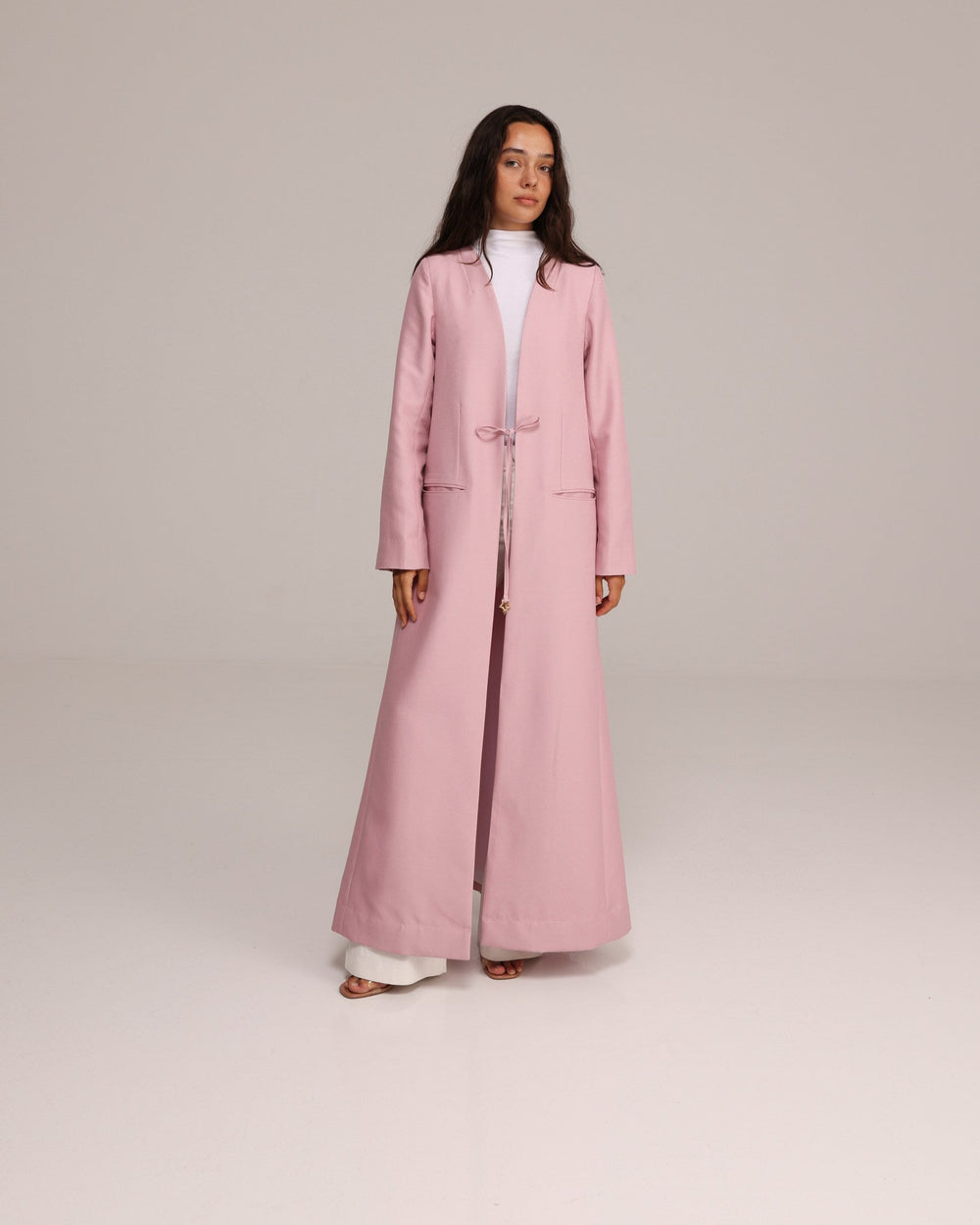 Woman wearing a long pink coat on a plain background