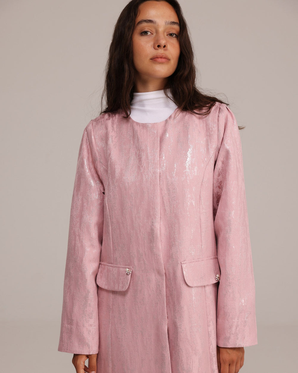 Woman wearing a pink coat over a white shirt against a plain background