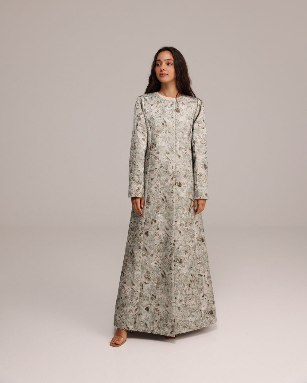 Woman wearing a long, light-colored dress with a subtle pattern on a plain background