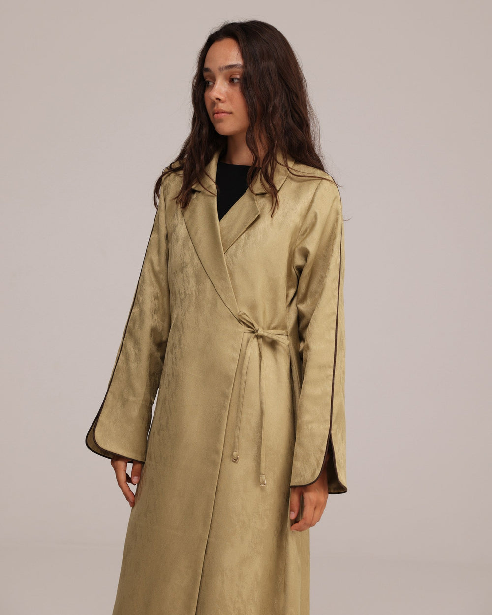 Woman wearing a beige trench coat against a plain background