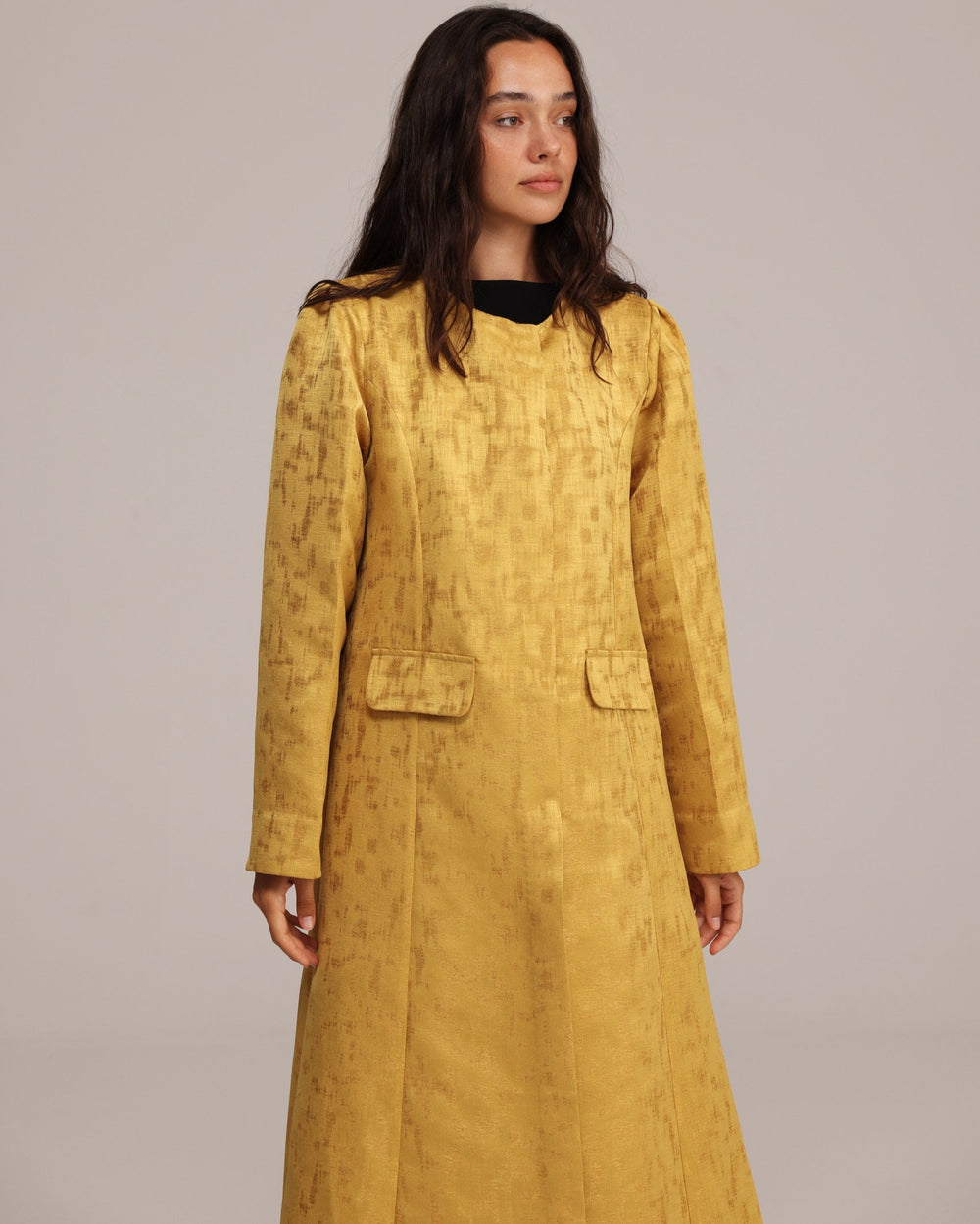 Woman wearing a mustard yellow textured dress against a plain background