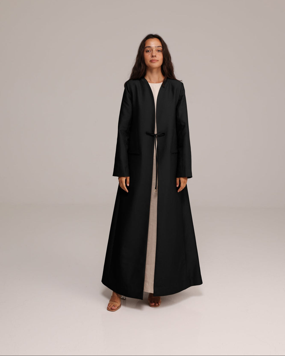 Woman wearing a long black coat on a plain background