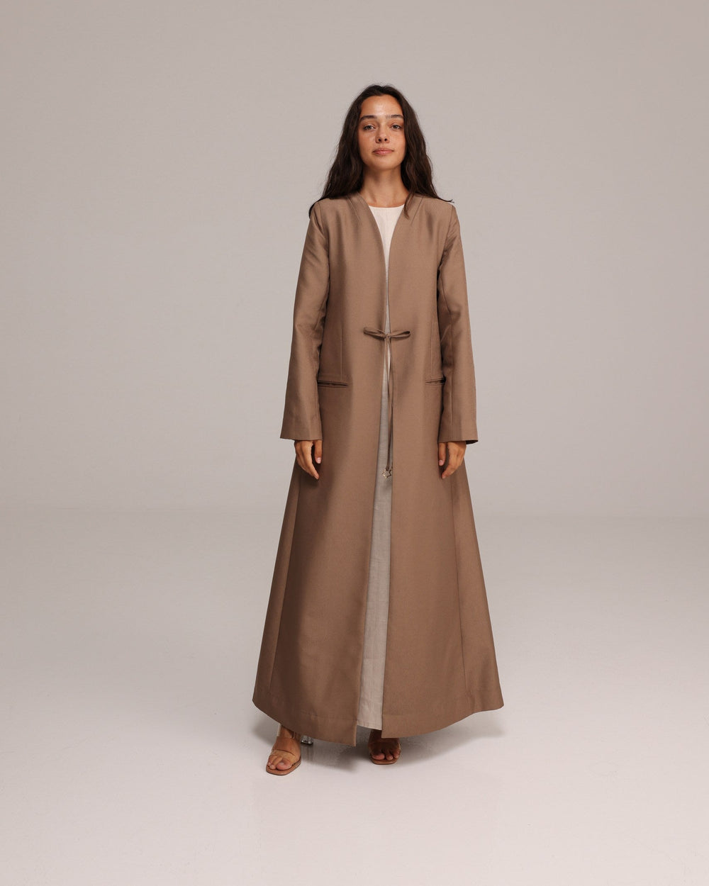 Woman wearing a long brown coat on a plain background