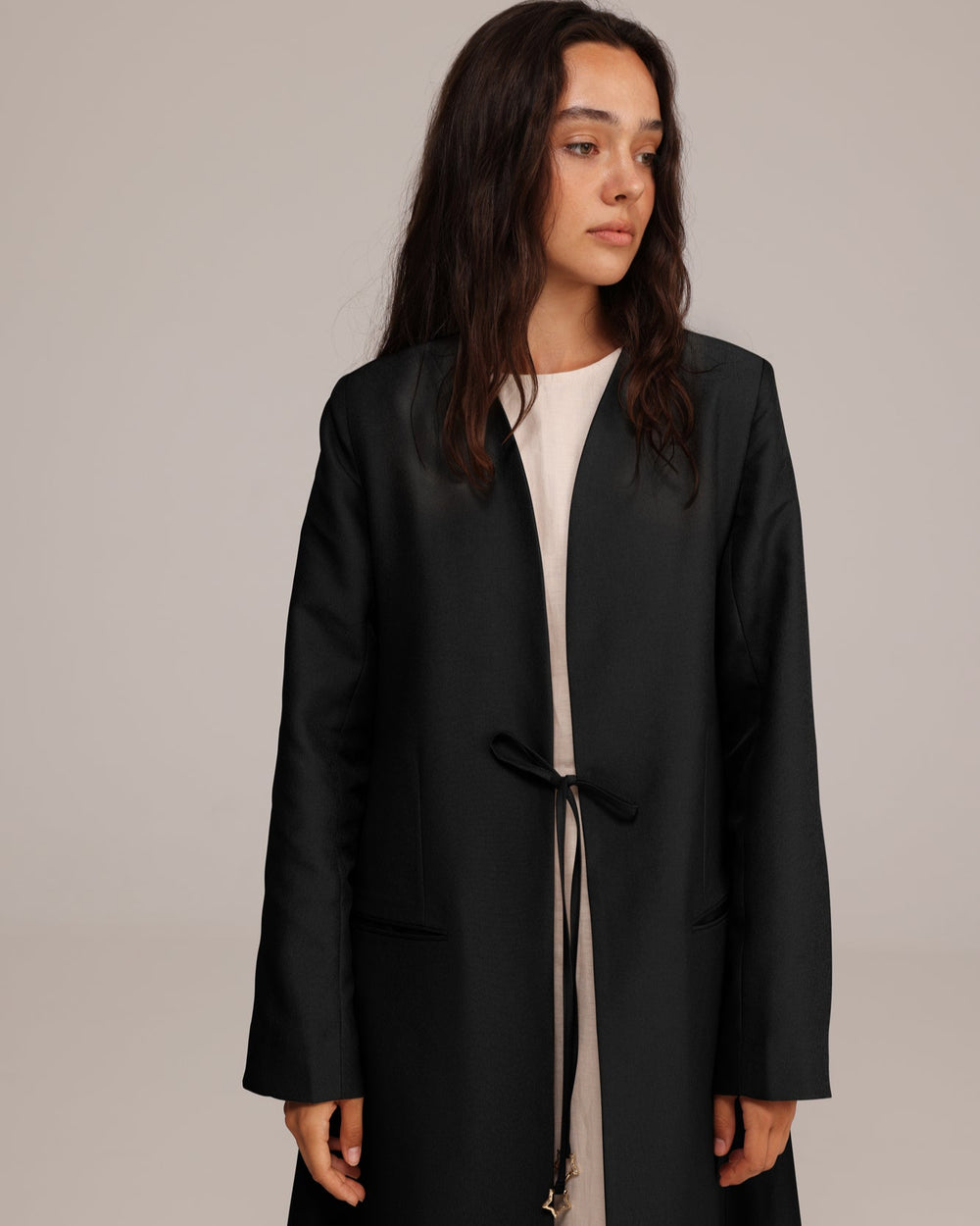 Woman wearing a black coat over a white shirt on a plain background