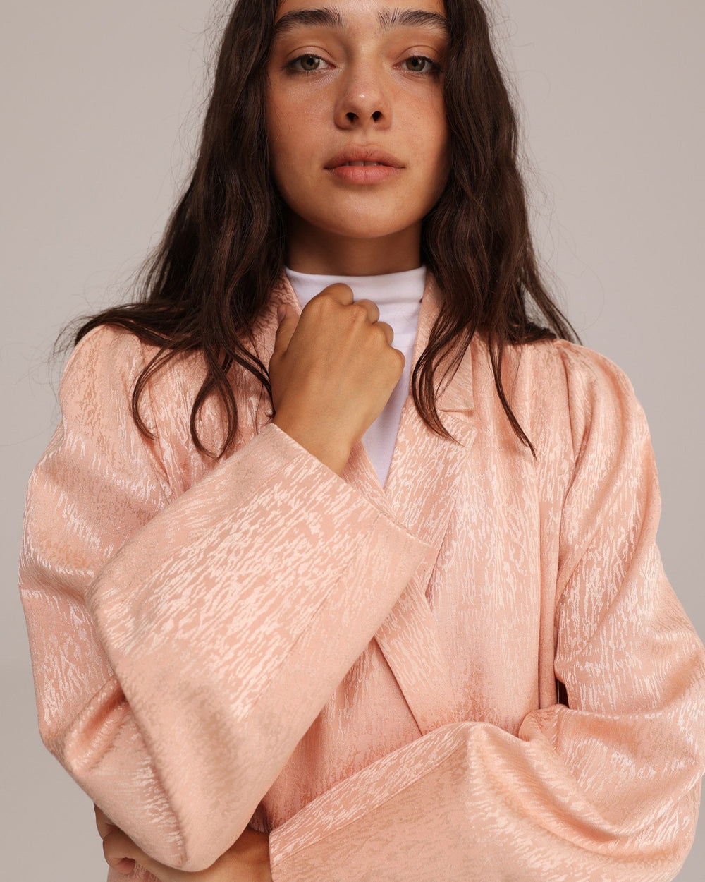 Woman wearing a light pink textured cardigan over a white shirt against a plain background